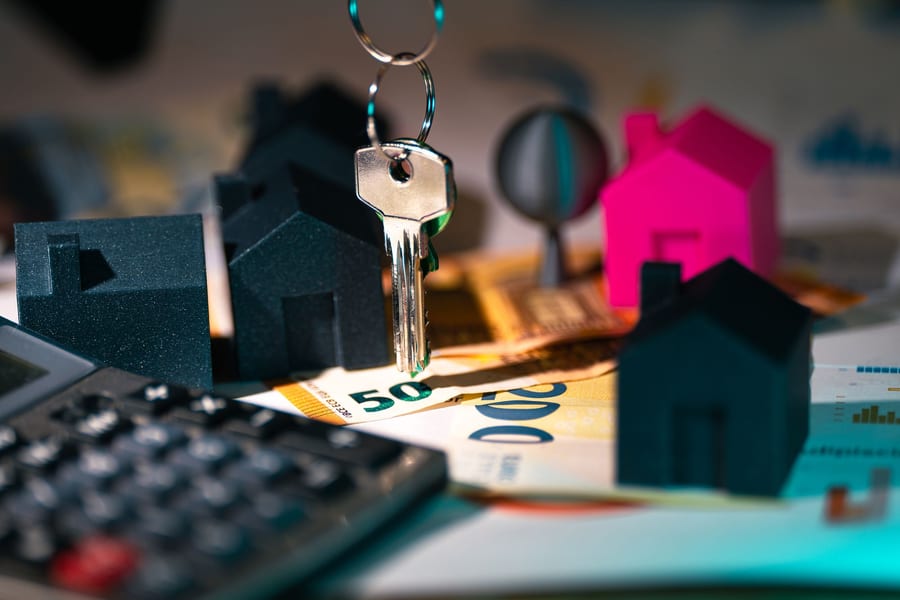 Chave sobre notas de euro, com miniaturas de casas e uma calculadora