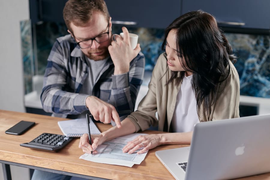 Casal sentado à mesa a rever contas com uma calculadora e um portátil